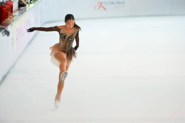 Mavi elbiseli yetenekli artistik patinajcı zarif bir şekilde karmaşık bir duruş sergiliyor.