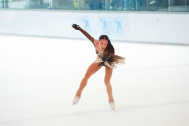 Mavi elbiseli yetenekli artistik patinajcı zarif bir şekilde karmaşık bir duruş sergiliyor.