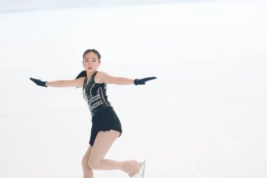 Mavi elbiseli yetenekli artistik patinajcı zarif bir şekilde karmaşık bir duruş sergiliyor.