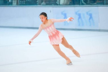 Mavi elbiseli yetenekli artistik patinajcı zarif bir şekilde karmaşık bir duruş sergiliyor.