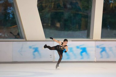 Mavi elbiseli yetenekli artistik patinajcı zarif bir şekilde karmaşık bir duruş sergiliyor.