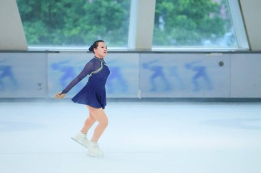 Mavi elbiseli yetenekli artistik patinajcı zarif bir şekilde karmaşık bir duruş sergiliyor.