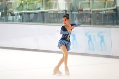 Mavi elbiseli yetenekli artistik patinajcı zarif bir şekilde karmaşık bir duruş sergiliyor.