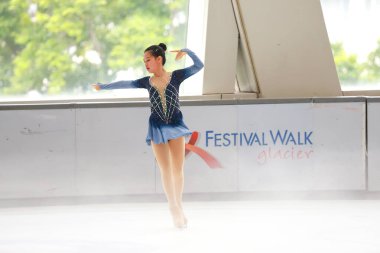 Mavi elbiseli yetenekli artistik patinajcı zarif bir şekilde karmaşık bir duruş sergiliyor.