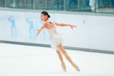 Mavi elbiseli yetenekli artistik patinajcı zarif bir şekilde karmaşık bir duruş sergiliyor.