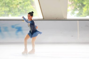 Mavi elbiseli yetenekli artistik patinajcı zarif bir şekilde karmaşık bir duruş sergiliyor.