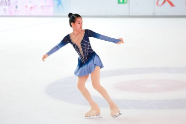 Mavi elbiseli yetenekli artistik patinajcı zarif bir şekilde karmaşık bir duruş sergiliyor.