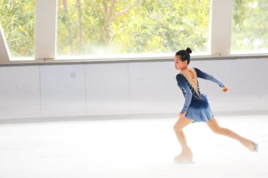 Mavi elbiseli yetenekli artistik patinajcı zarif bir şekilde karmaşık bir duruş sergiliyor.