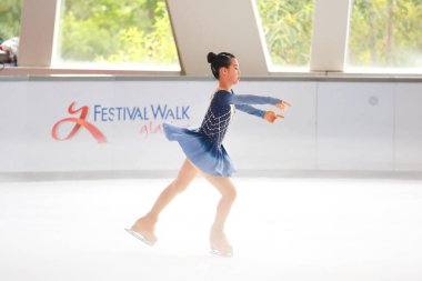 Mavi elbiseli yetenekli artistik patinajcı zarif bir şekilde karmaşık bir duruş sergiliyor.