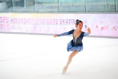 Mavi elbiseli yetenekli artistik patinajcı zarif bir şekilde karmaşık bir duruş sergiliyor.