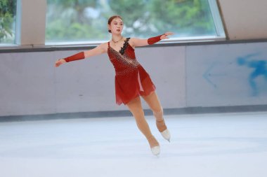 Mavi elbiseli yetenekli artistik patinajcı zarif bir şekilde karmaşık bir duruş sergiliyor.