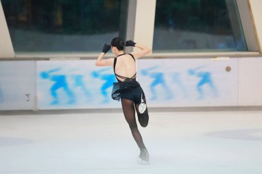 Mavi elbiseli yetenekli artistik patinajcı zarif bir şekilde karmaşık bir duruş sergiliyor.