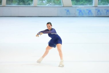 Mavi elbiseli yetenekli artistik patinajcı zarif bir şekilde karmaşık bir duruş sergiliyor.