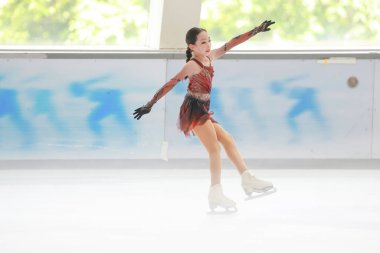 Mavi elbiseli yetenekli artistik patinajcı zarif bir şekilde karmaşık bir duruş sergiliyor.