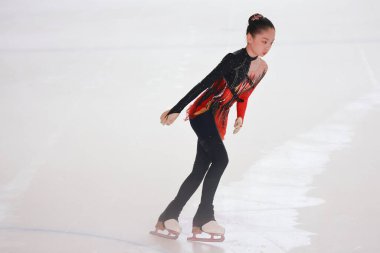 Mavi elbiseli yetenekli artistik patinajcı zarif bir şekilde karmaşık bir duruş sergiliyor.