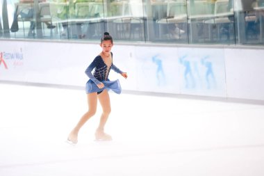 Mavi elbiseli yetenekli artistik patinajcı zarif bir şekilde karmaşık bir duruş sergiliyor.