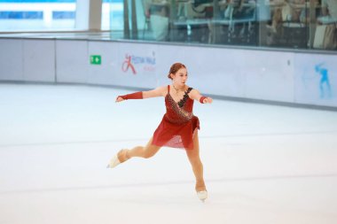 Mavi elbiseli yetenekli artistik patinajcı zarif bir şekilde karmaşık bir duruş sergiliyor.