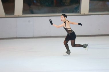 Mavi elbiseli yetenekli artistik patinajcı zarif bir şekilde karmaşık bir duruş sergiliyor.