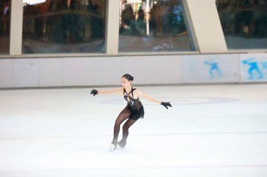 Mavi elbiseli yetenekli artistik patinajcı zarif bir şekilde karmaşık bir duruş sergiliyor.