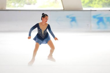 Mavi elbiseli yetenekli artistik patinajcı zarif bir şekilde karmaşık bir duruş sergiliyor.