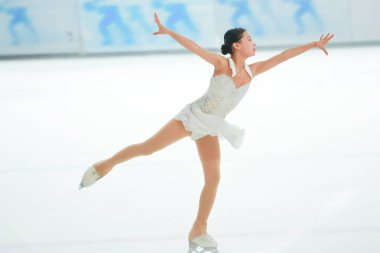 Mavi elbiseli yetenekli artistik patinajcı zarif bir şekilde karmaşık bir duruş sergiliyor.