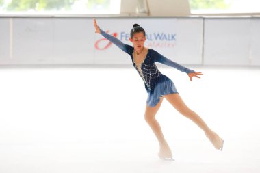 Mavi elbiseli yetenekli artistik patinajcı zarif bir şekilde karmaşık bir duruş sergiliyor.