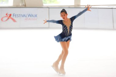 Mavi elbiseli yetenekli artistik patinajcı zarif bir şekilde karmaşık bir duruş sergiliyor.