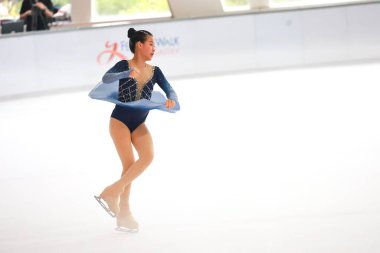 Mavi elbiseli yetenekli artistik patinajcı zarif bir şekilde karmaşık bir duruş sergiliyor.