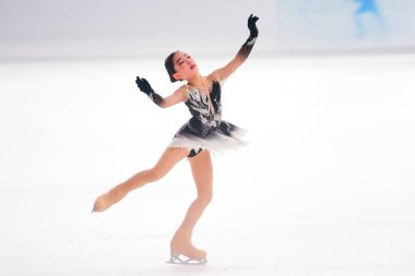 Mavi elbiseli yetenekli artistik patinajcı zarif bir şekilde karmaşık bir duruş sergiliyor.