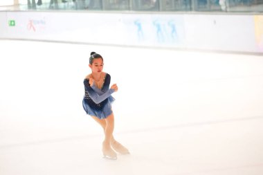 Mavi elbiseli yetenekli artistik patinajcı zarif bir şekilde karmaşık bir duruş sergiliyor.