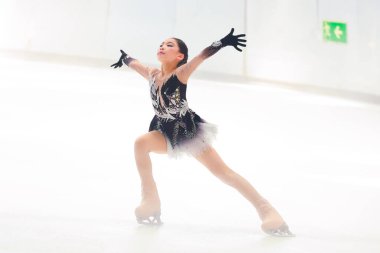 Mavi elbiseli yetenekli artistik patinajcı zarif bir şekilde karmaşık bir duruş sergiliyor.