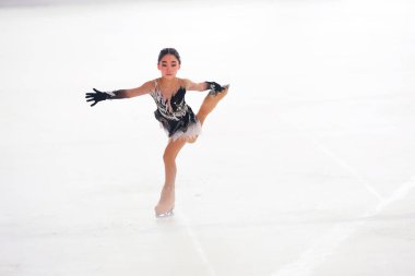 Mavi elbiseli yetenekli artistik patinajcı zarif bir şekilde karmaşık bir duruş sergiliyor.