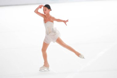 Mavi elbiseli yetenekli artistik patinajcı zarif bir şekilde karmaşık bir duruş sergiliyor.