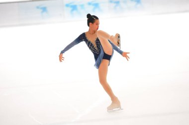 Mavi elbiseli yetenekli artistik patinajcı zarif bir şekilde karmaşık bir duruş sergiliyor.