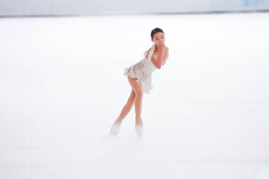 Mavi elbiseli yetenekli artistik patinajcı zarif bir şekilde karmaşık bir duruş sergiliyor.