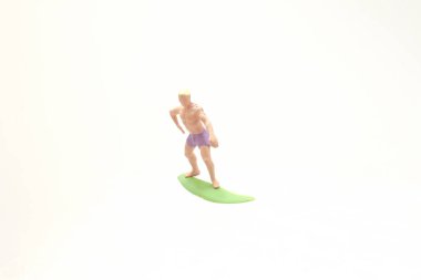 Mor şort giyen küçük bir plastik sörfçü heykeli.