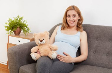 Oyuncak ayı tutan hamile bir kadın.