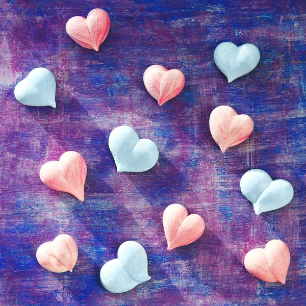 pink and blue meringue hearts on painted purple background diagonally, square
