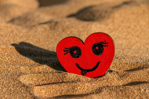 painted black smiling face on red wooden heart and yellow sand on beach, sunny day, love symbol