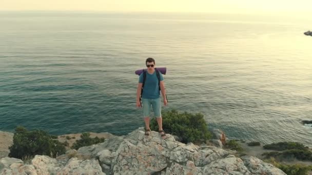 Человек с рюкзаком стоит на скале — стоковое видео