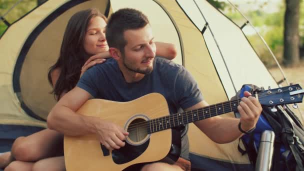 Man gitaarspelen voor zijn vriendin zit op de camping tent — Stockvideo