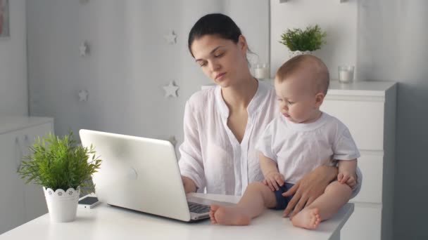 Madre cansada con el bebé trabajando en el ordenador portátil — Vídeos de Stock