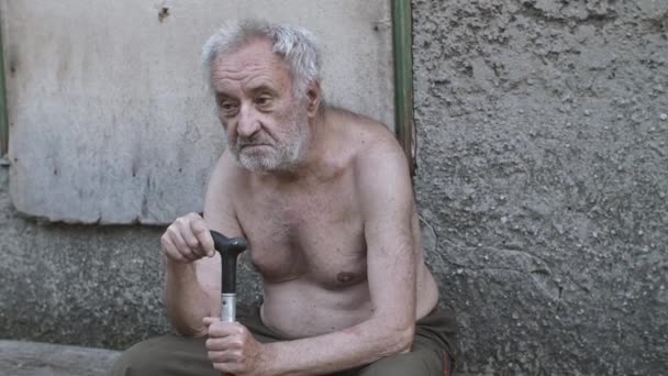 Ledsen gammal tiggaren man med en käpp sitter på gatan — Stockvideo