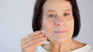 Yaşlı kadın pamuk ped ile yüzünü temizler