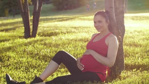 Une femme enceinte assise sur l'herbe et rêvant — Video