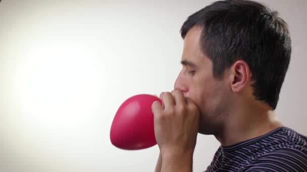 Hombre soplando globo rojo sobre fondo blanco — Vídeo de stock