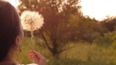 Kadın gün batımında karahindiba üflüyor.
