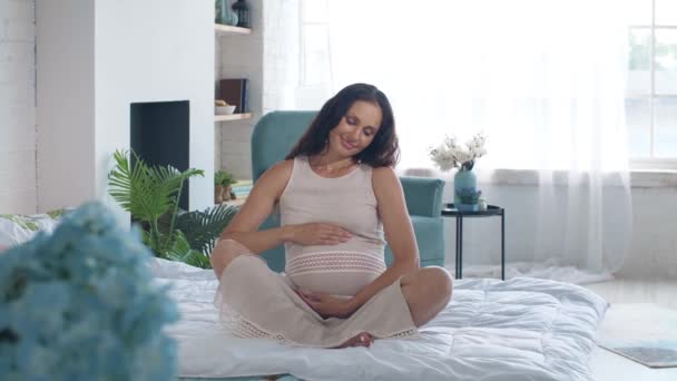 Femme enceinte sur un lit caresse son ventre — Video