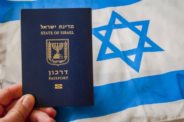 Hand holding the passport of the State of Israel, Israeli flag on the background. Israel citizenship concept, Israeli \