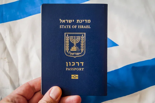 Hand holding the passport of the State of Israel, Israeli flag on the background. Israel citizenship concept, Israeli \